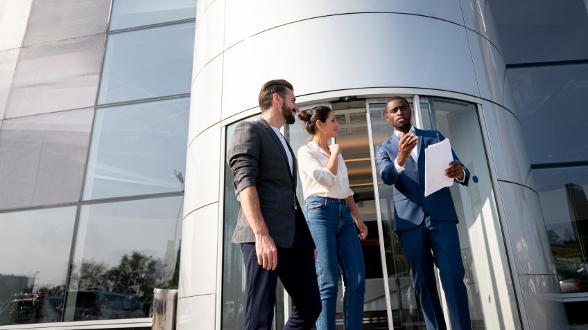 Portrait of a happy salesman selling a car to a couple at the dealership â lifestyle concepts.
