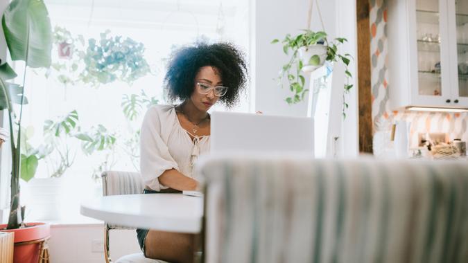 A happy young adult woman enjoys time working from home, the house interior well designed and decorated with an assortment of interesting plants.