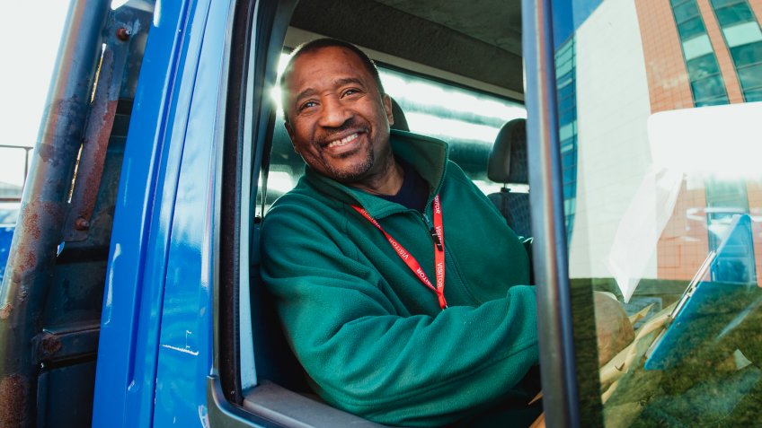 Senior truck driver is smiling while pulling out of a parking lot in his work truck.