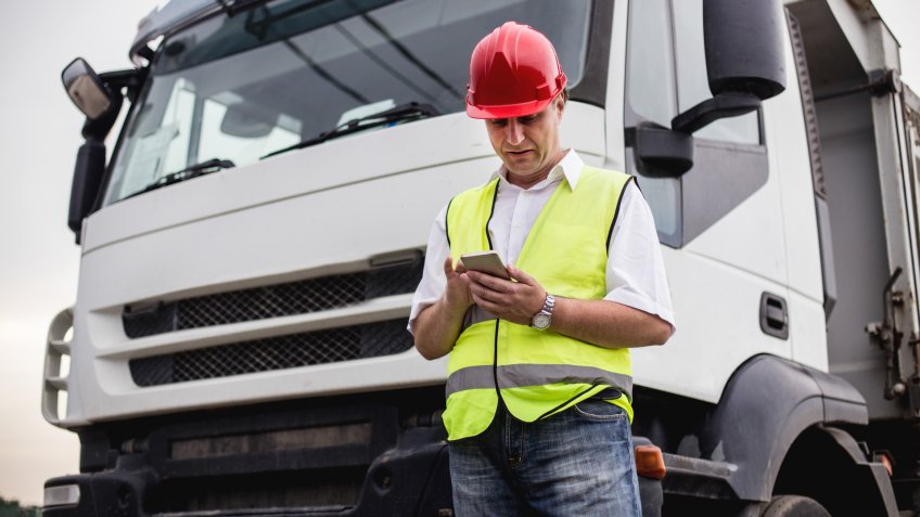 Truck driver or construction worker us ing a mobile app next to a truck.