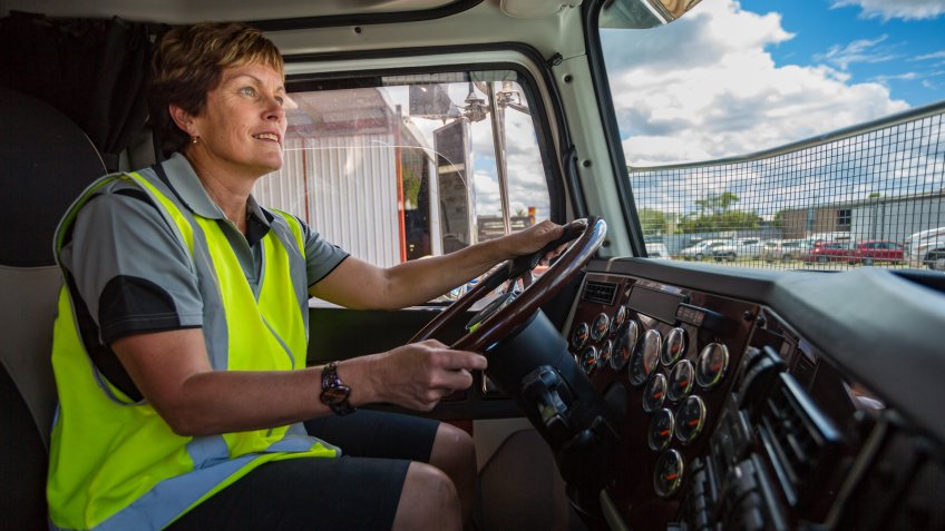 Empowered happy woman driving a truck in the transport industry wearing high visibility clothing.