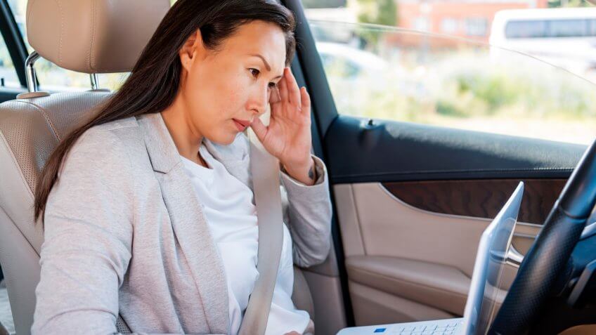 Elegant Asian business lady sitting in car and working on laptop.