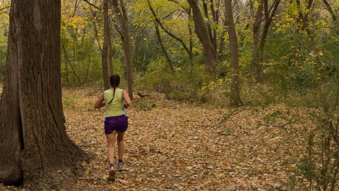 On a humid, fall day, a woman with a ponytail in shorts and t-shirt runs on the colorful carpet of leaf littler under large yellow trees in Sparger Park in the suburb of Colleyville, Dallas Texas.