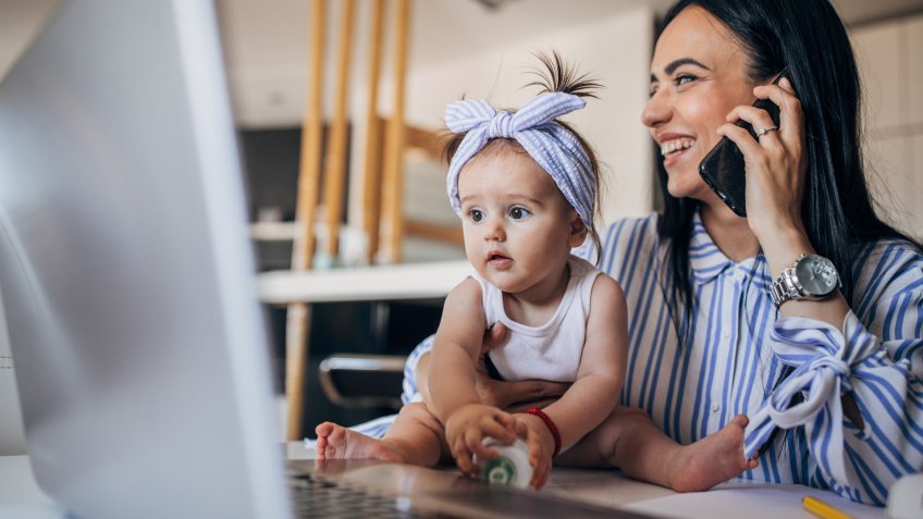 Mother and baby girl working on laptop and using phone.