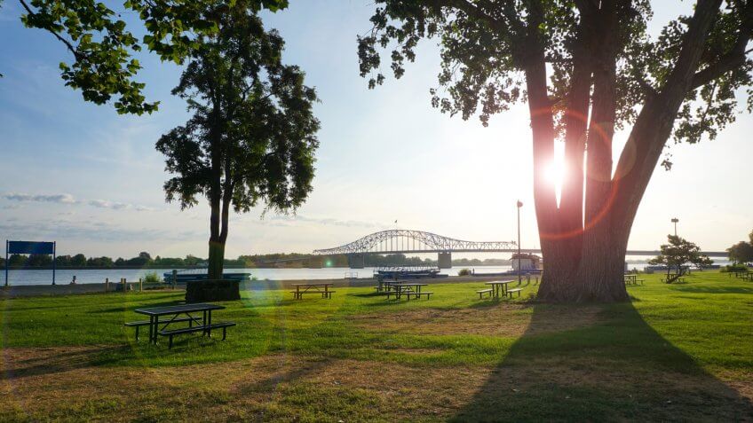 Park on Columbia river in Washington State with bright sun flare and bridge in background.