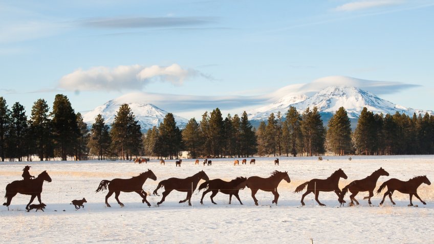 A metal scurpture of two cowboys and a string of horses with the three sisters mountains in backgroundnear Sisters, Oregon.