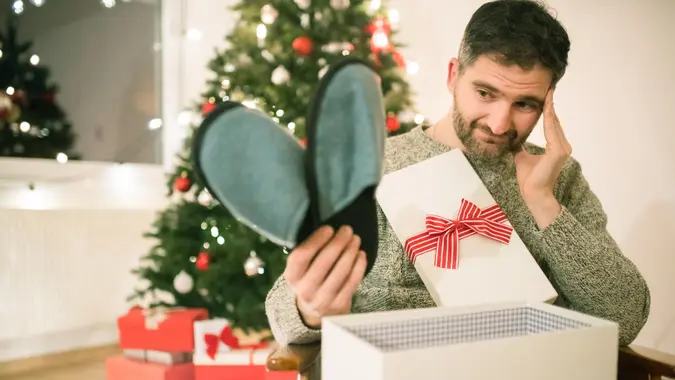 Caucasian man opening a Christmas present with disappointment.