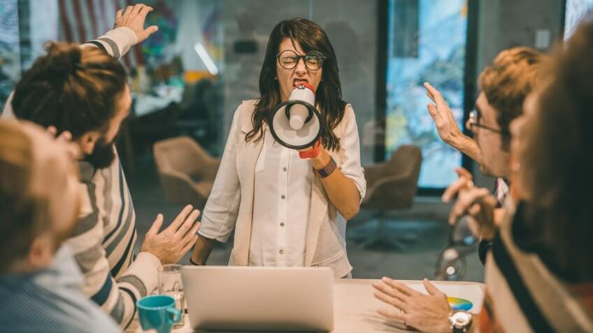 Angry female manager yelling at her team through megaphone in the office.