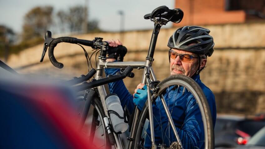 A senior man is removing his racing bike from his car bike rack.