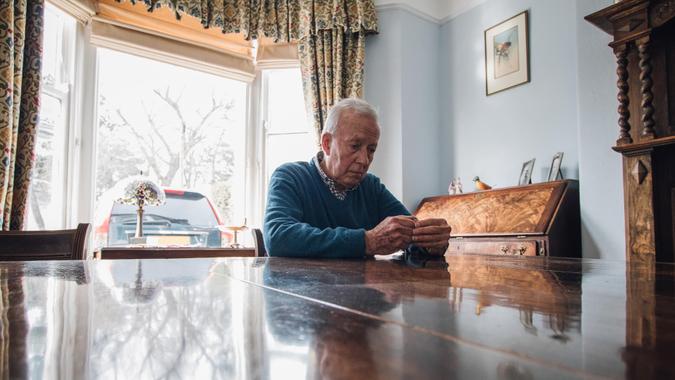 Senior man is sitting alone at the dining table in his home, with a worried expression on his face.