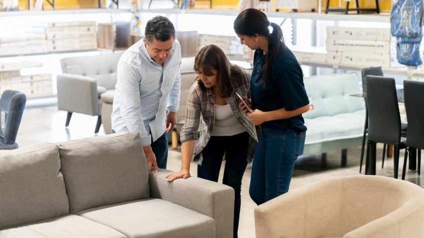 Happy couple buying a couch at a home improvement store and talking to a saleswoman - business concepts.
