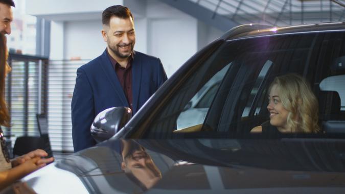 Consultant helping woman and kids to get inside of new car while testing it in dealer shop.