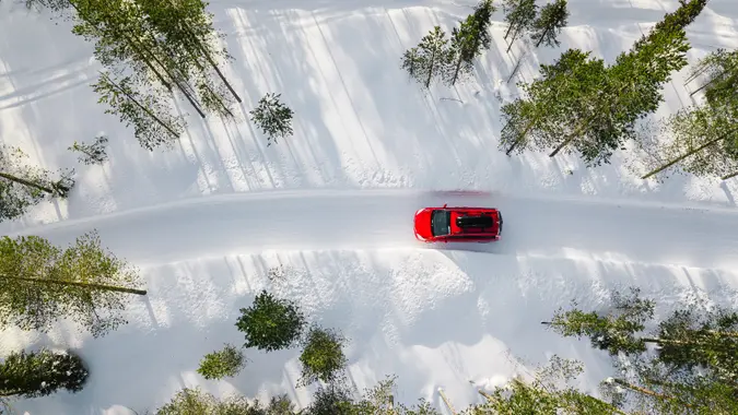 Aerial view of red car driving through the white snow winter forest on country road in Finland, Lapland.