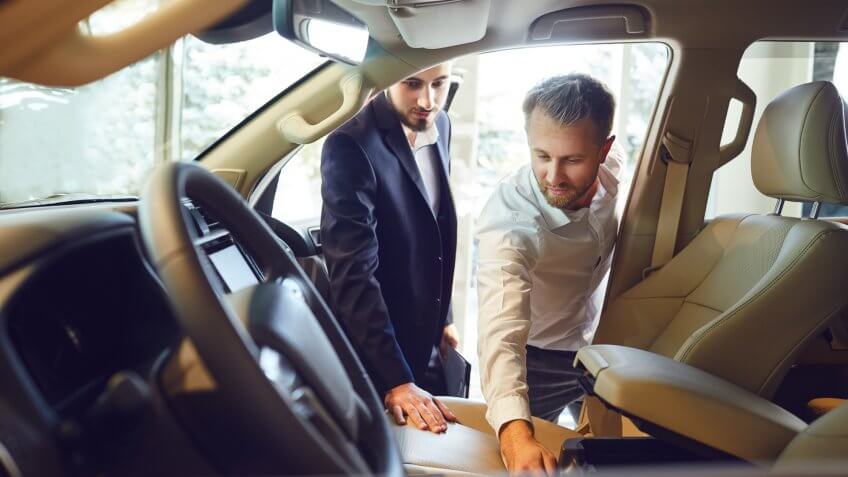 Professional salesmen selling cars at dealership to buyer.