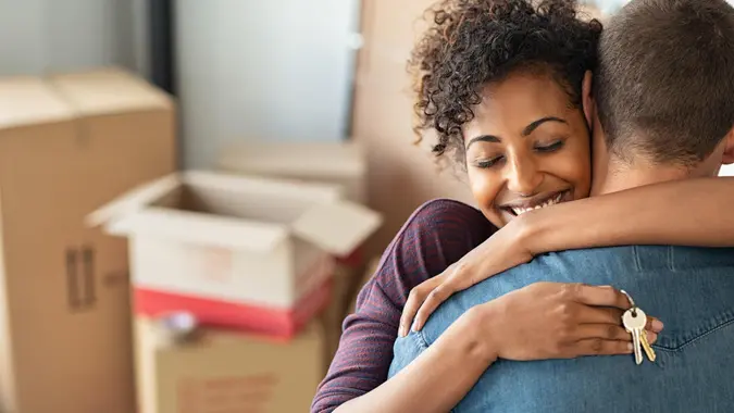 Young african woman holding home keys while hugging boyfriend in their new apartment after buying real estate.