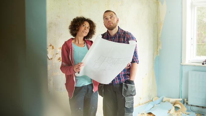 a young couple take time out from scraping walls in her new house to check against their architect plans.