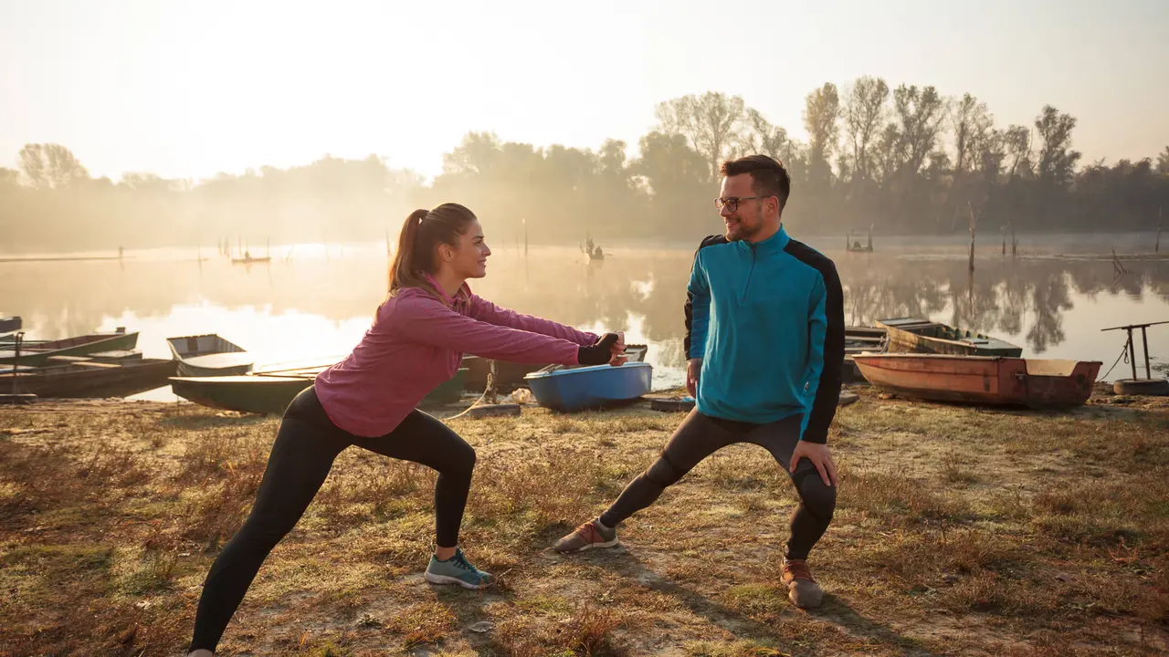 Beautiful young man and woman exercising, stretching in the early morning mist on the lake or river banks.