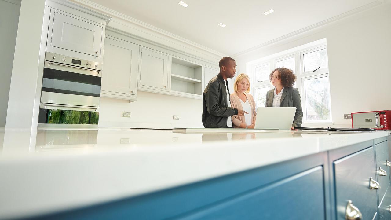 a saleswoman or estate agent shows a couple around a home with new kitchen.
