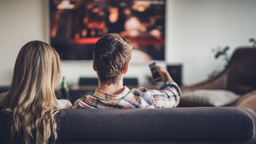 Back view of a couple watching TV on sofa in the living room.