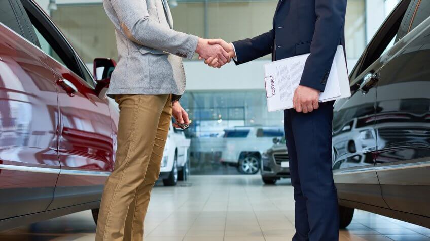 Low section side view of handsome client shaking hands with sales manager in car showroom, after buying brand new luxury car.