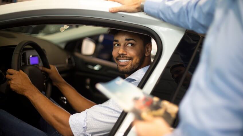 Car salesperson showing the new car model features to a customer in an automotive dealership.