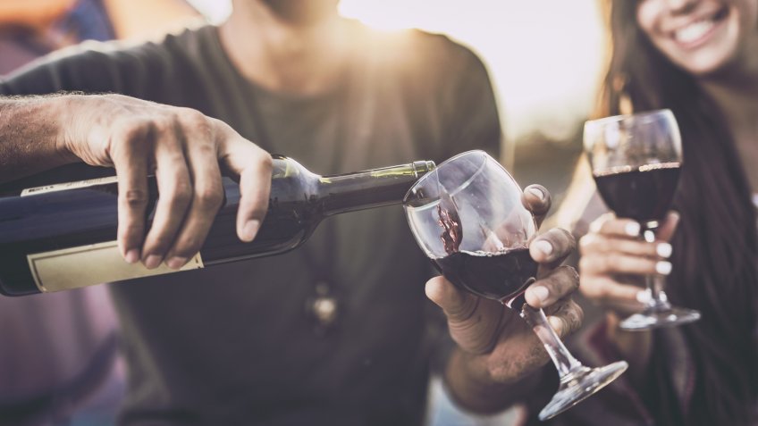 Close up of a couple drinking wine outdoors while man is pouring it into a glass.