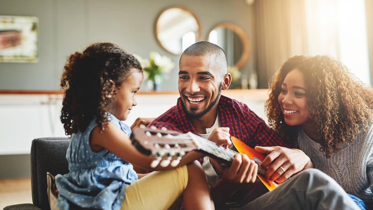 Shot of an adorable little girl and her parents playing a guitar together on the sofa at home.
