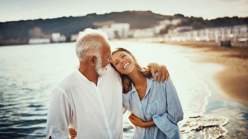 Grandfather and his granddaughter walking on the beach during family summer vacation.