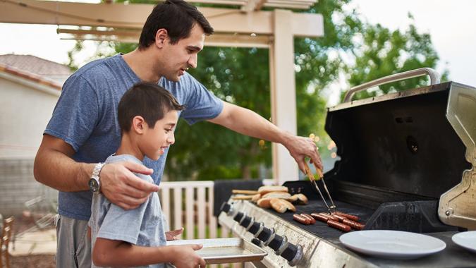 father teaching son how to grill hot dogs and bonding during the day.