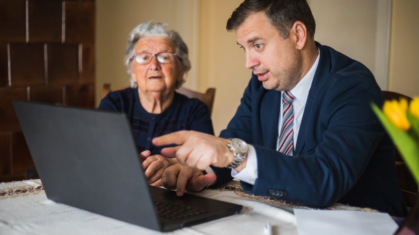 Man in business suit showing something on laptop to old lady.