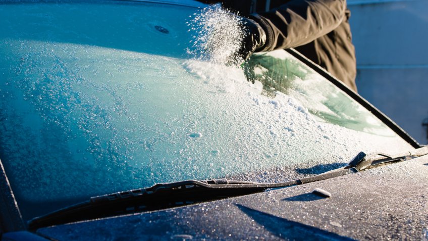 A man cleans frozen windshield by scratching, cold morning.