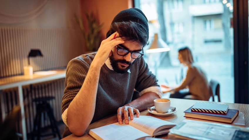 Young bearded man studying alone in a coffee shop.