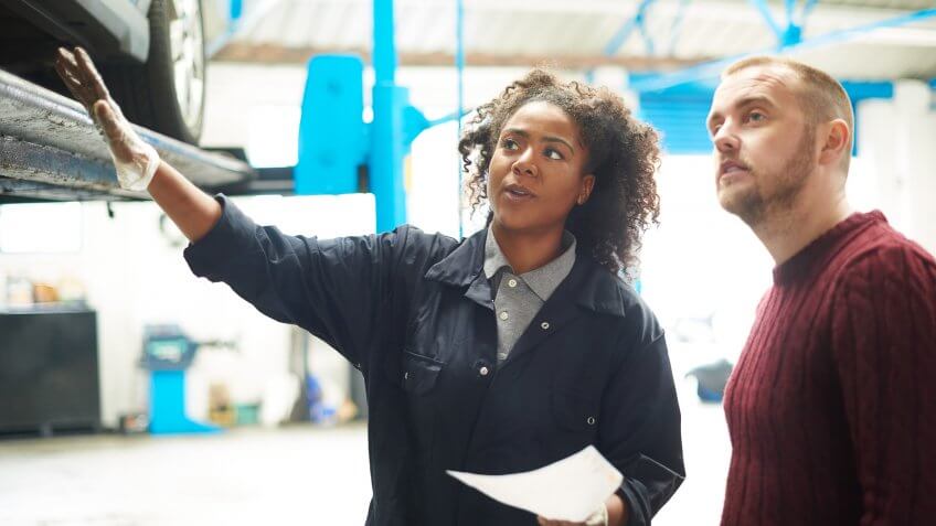 A female garage mechanic is standing with a customer in her garage and is explaining the itemised bill to him .