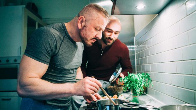 homosexual couple stands together in the kitchen at the stove and tasting the meal.