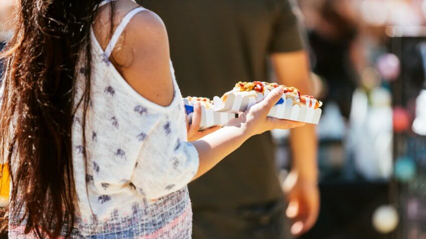 Woman holds two hot dogs at a food fair.