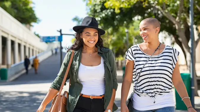 Young smiling women walking and talking while looking at each other outdoor.