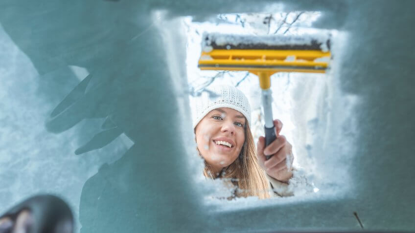 girl scraping icy windshield on car