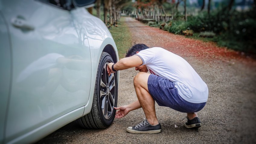 Young asian man checking car air tire while travel at Countryside.