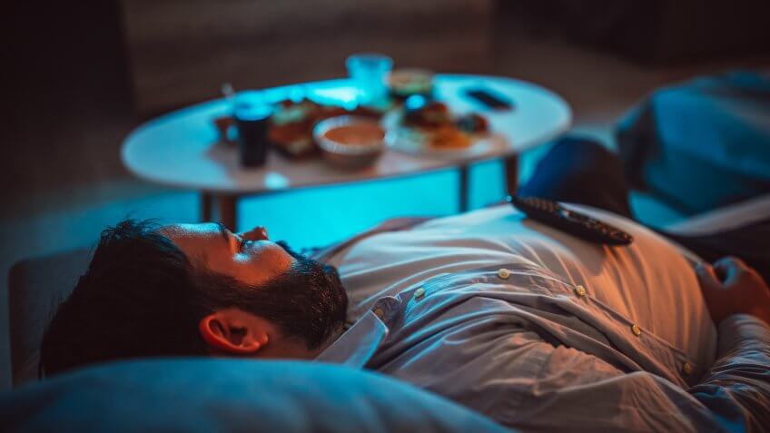 Overweight guy, lying on sofa, with junk food in front of him.