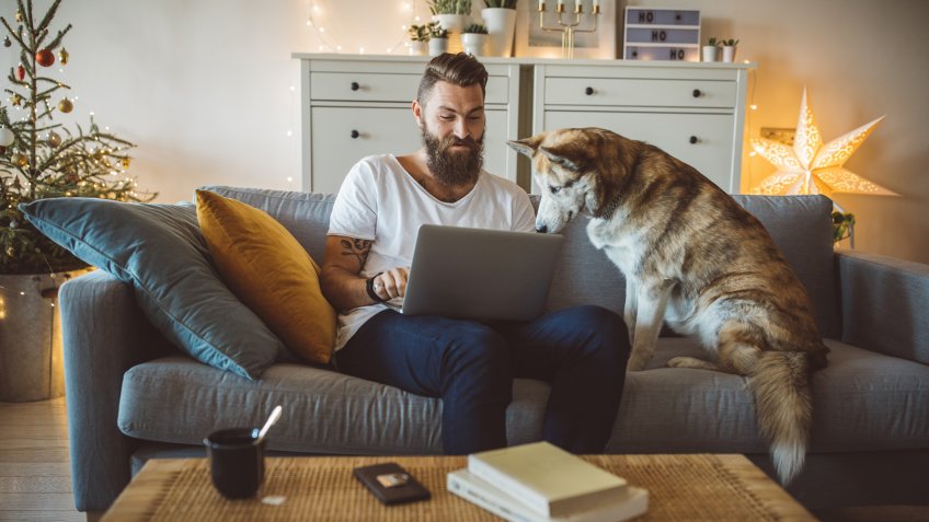 Young men celebrating Christmas at home, he sitting on bed and using laptop.
