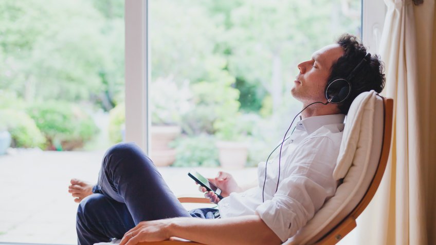 listening relaxing music at home, relaxed man in headphones sitting in deck chair in modern bright interior.