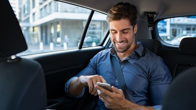 Happy smiling businessman man typing message on phone while sitting in a taxi.