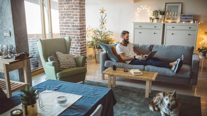 Young men celebrating Christmas at home, he sitting on bed and using laptop.