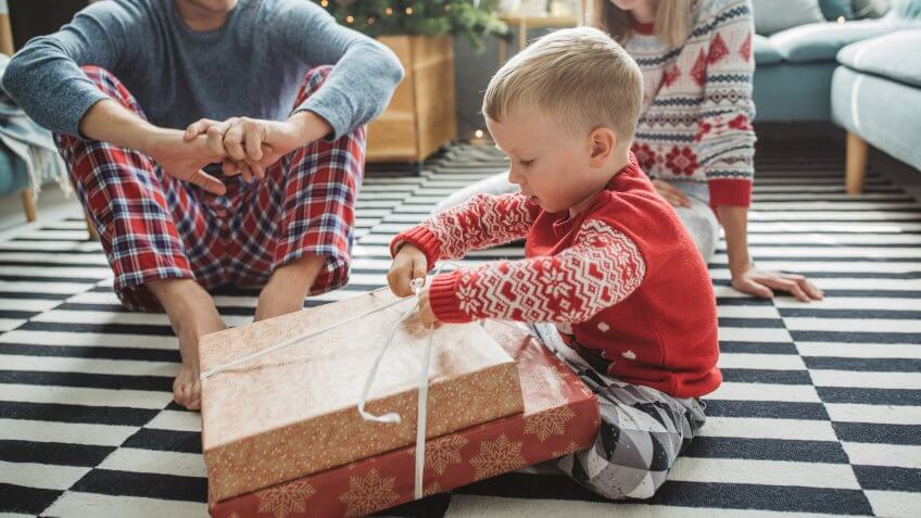 Young parents with baby boy celebrating Christmas at home, boy opening presents .