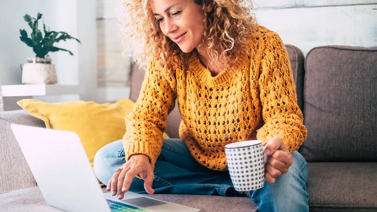 Nice beautiful lady with blonde curly hair work at the notebook sit down on the sofa at home - check on line shops for cyber monday sales - technology woman concept for alternative office freelance.
