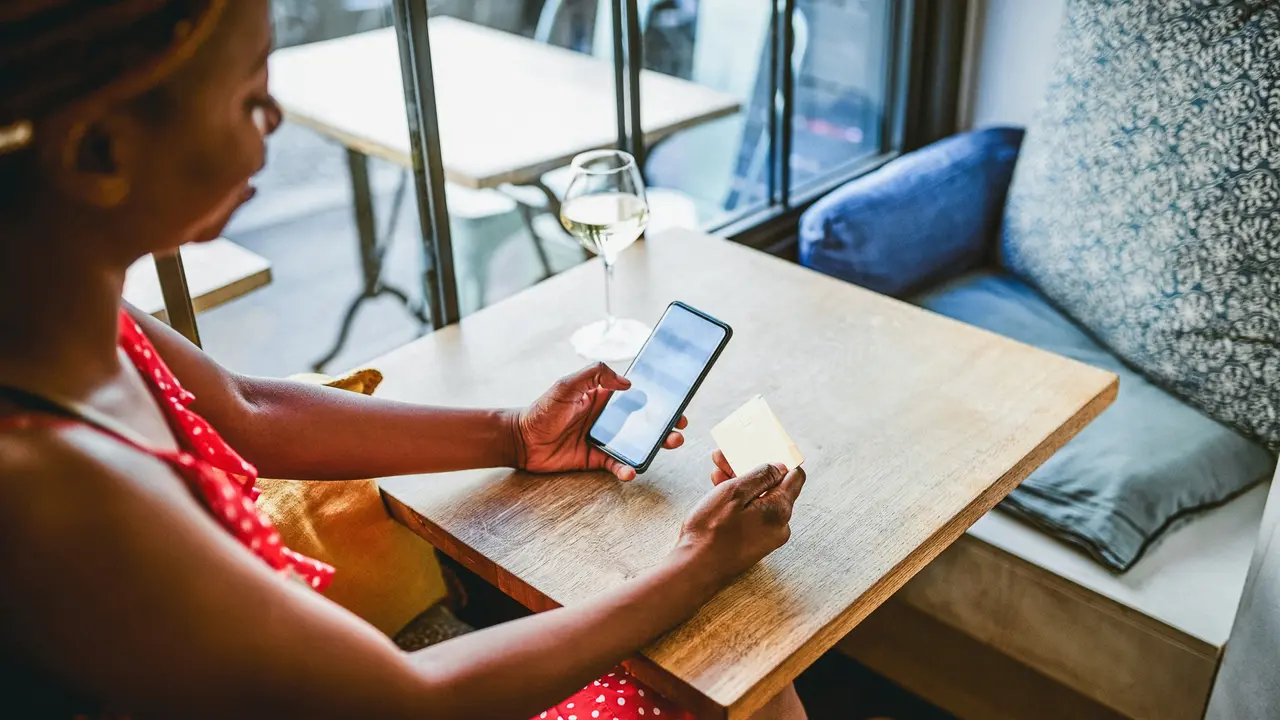 High angle shot of an attractive young woman using her credit card and cellphone while relaxing inside a cafe.