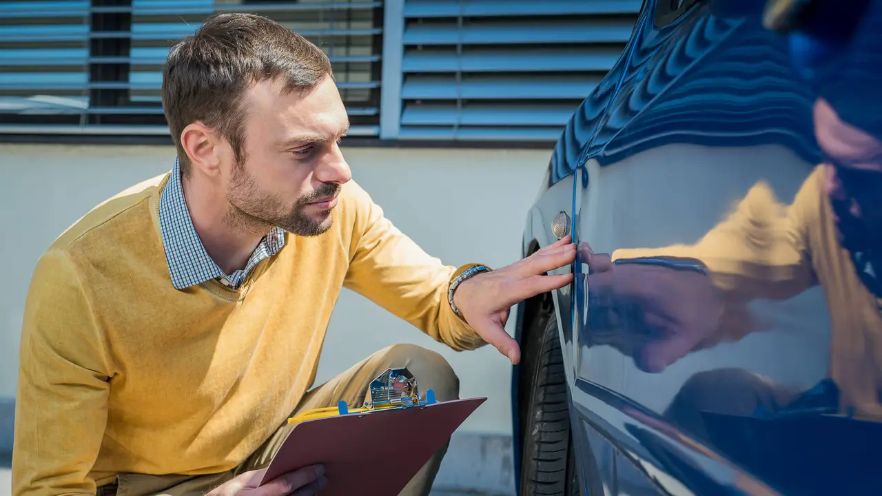 An insurance agent inspects a car after an accident.