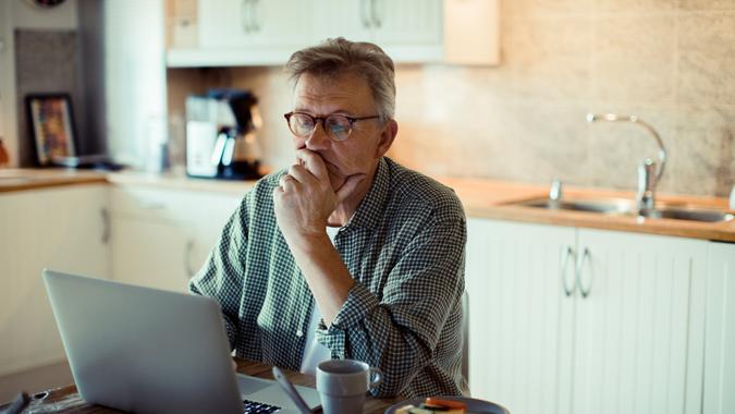 Close up of a mature man using a laptop at home while having breakfast.