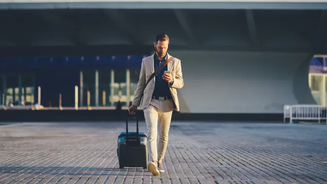 Young businessman with suitcase just arriving in Valencia and texting on phone.