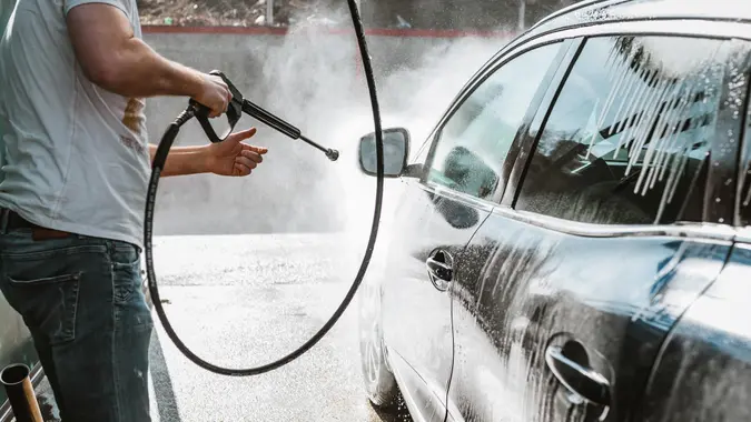 Man, washing his car in the stall of a car wash, using a high pressure water jet .